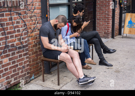 Les gens branchés préoccupés avec leur smartphone en dehors d'un café dans le quartier branché de Williamsburg Brooklyn de quartier hipster Banque D'Images