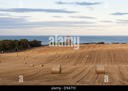 Hay bails dans un champ les agriculteurs sur la magnifique côte de Northumberland avec la mer et une église en arrière-plan Banque D'Images