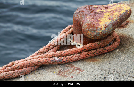 Ancienne borne d'amarrage rouillées avec marine rouge sur corde jetée en béton Banque D'Images