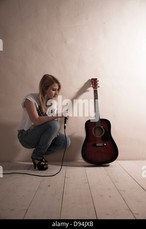 Woman Crouching avec Microphone à côté de guitare Banque D'Images