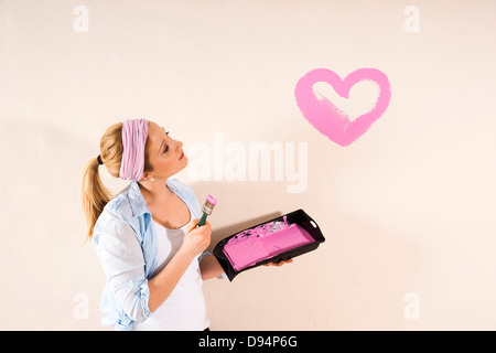 Studio Shot of Young Woman Painting Heart on Wall Banque D'Images