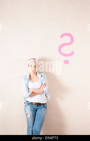 Studio Shot of Young Woman Leaning Against Wall with Question Mark Banque D'Images