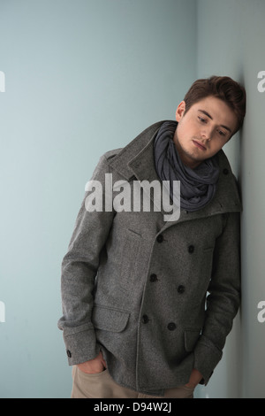 Portrait de jeune homme portant un foulard gris et veste, Leaning against Wall, Studio Shot sur fond gris Banque D'Images