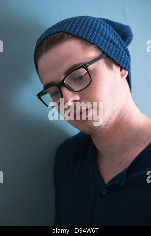 Close-up Portrait of Young Man wearing Woolen Hat et Horn-rimmed lunettes, à la baisse, Studio Shot on Blue Background Banque D'Images