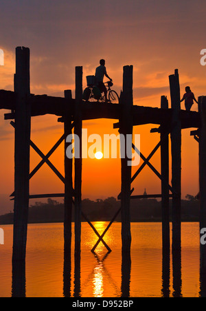 Les Birmans utilisent le pont en teck U BEINS de commuer à travers le lac Taungthaman au lever du soleil - AMARAPURA, MYANMAR Banque D'Images