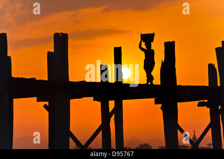 Les Birmans utilisent le pont en teck U BEINS de commuer à travers le lac Taungthaman au lever du soleil - AMARAPURA, MYANMAR Banque D'Images