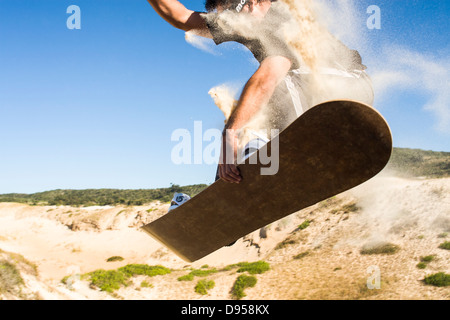 Sandboarder jumping and holding sa board sur les dunes de Ribanceira Beach. Banque D'Images