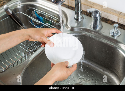 Photo horizontale des mains rincer une petite assiette blanche avec un évier et robinet d'exécution en arrière-plan Banque D'Images