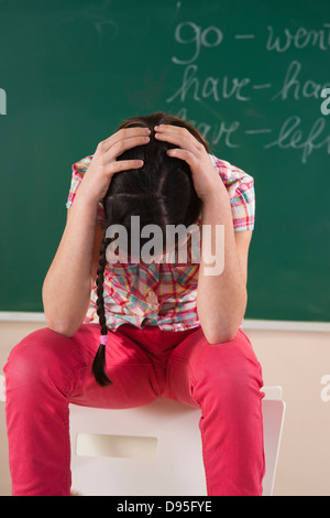 Fille avec les mains sur la tête en avant du tableau en classe Banque D'Images