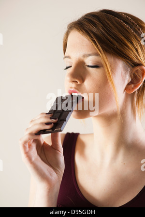 Teenage Girl Eating chocolate with Eyes Closed, Studio Shot on White Background Banque D'Images