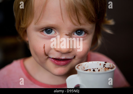 3 ans garçon boit du lait chaud et le chocolat avec une cuillère dans un café où sa mère a coffee Banque D'Images