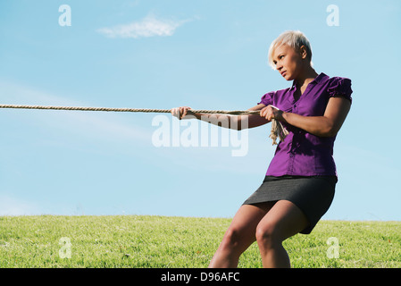 Resolute business woman pulling rope contre ciel bleu, symbole de puissance et de détermination. L'espace de copie, side view Banque D'Images