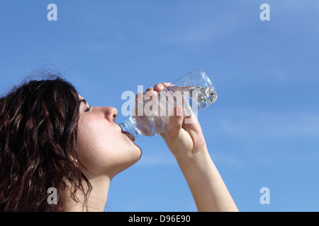 Profil d'une belle femme l'eau potable à partir d'une bouteille en plastique avec un ciel bleu en arrière-plan Banque D'Images