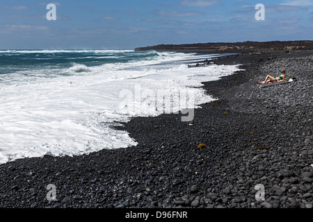 Femme en train de bronzer sur une plage de rochers volcaniques, Playa Vista Papagayo, Lanzarote, îles Canaries, Espagne Banque D'Images