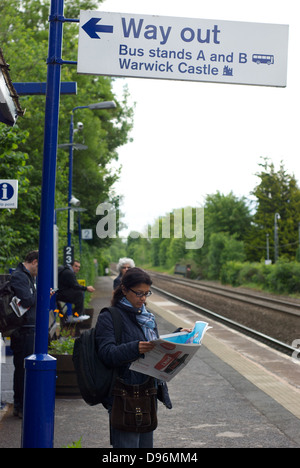 Une femme attend un train de voyageurs sur la plate-forme en direction de Warwick Gare lire un journal Banque D'Images