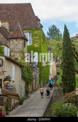 Les touristes à pied jusqu'charmant en pente pavées étroites rue bordée de boutiques à Sarlat, Dordogne France Banque D'Images