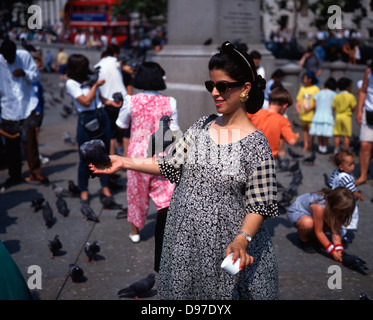 1994. Une femme dans l'alimentation à la main des lunettes de grain pour les pigeons à Trafalgar square, occupé avec d'autres personnes de faire la même à proximité. Londres, Angleterre, Royaume-Uni. Banque D'Images