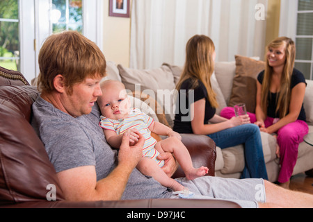 Père avec bébé garçon et deux jeunes femmes dans le salon de leur maison Banque D'Images