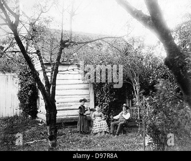 Cette photographie montre des homesteaders assis dans un jardin autour de leur cabane en rondins dans l'État de Washington. L'image date probablement du début des années 1900, représentant les premiers colons et leur mode de vie rural. Banque D'Images