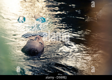 Femme flottant dans l'eau pendant le coucher du soleil Banque D'Images