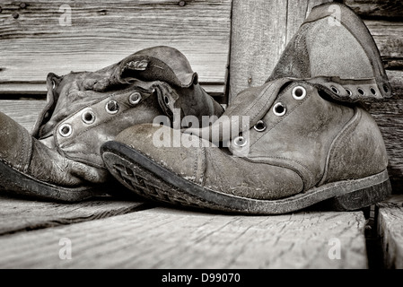 Photo noir et blanc de old weathered chaussures de randonnée sur le porche en bois de l'Emporium Chitina, ville isolée de Chitina, Alaska, USA Banque D'Images