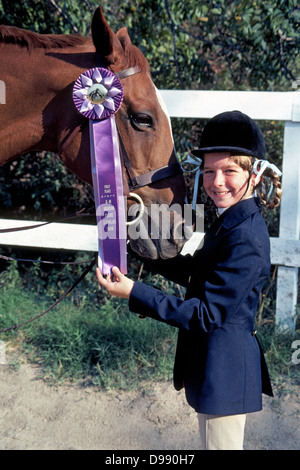 Une jeune fille en vêtements d'équitation et un casque heureusement affiche la première place elle ruban et son cheval a gagné à un spectacle équestre en Californie, USA. Banque D'Images