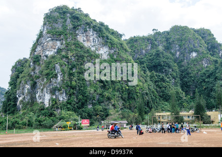 VIENG Xai, Laos — les étudiants spectateurs s'alignent sur leurs scooters et leurs vélos pour assister à un concours d'arbalètes sur un terrain de jeu en terre battue parmi le terrain accidenté près de Vieng Xai dans le nord-est du Laos. L’événement local attire des participants et des spectateurs des villages environnants de cette région rurale. Banque D'Images