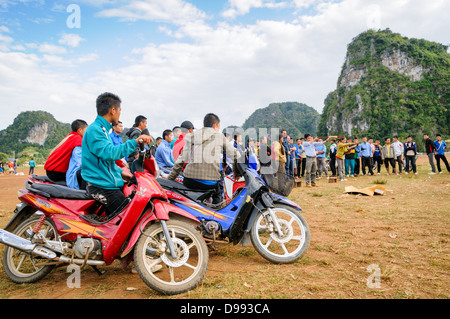 VIENG Xai, Laos — les étudiants spectateurs s'alignent sur leurs scooters et leurs vélos pour assister à un concours d'arbalètes sur un terrain de jeu en terre battue parmi le terrain accidenté près de Vieng Xai dans le nord-est du Laos. L’événement local attire des participants et des spectateurs des villages environnants de cette région rurale. Banque D'Images