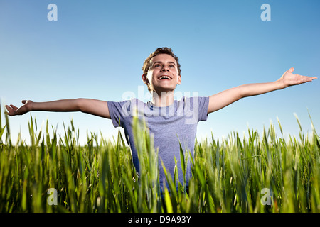 Portrait d'un adolescent dans un champ de blé vert au coucher du soleil contre le ciel bleu clair Banque D'Images