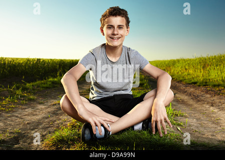 Portrait de plein air d'un adolescent garçon assis au milieu d'un chemin de terre en milieu rural Banque D'Images