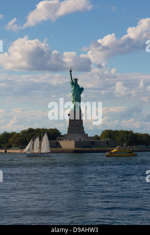 La Statue de la liberté sur Liberty Island, New York, NY, USA, avec un voilier et un bateau-taxi NYC en passant en face de lui. Banque D'Images