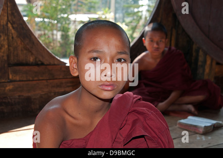 Novice deux moines bouddhistes en robe rouge assis les jambes croisées dans un monastère par fenêtre ronde Myanmar Banque D'Images