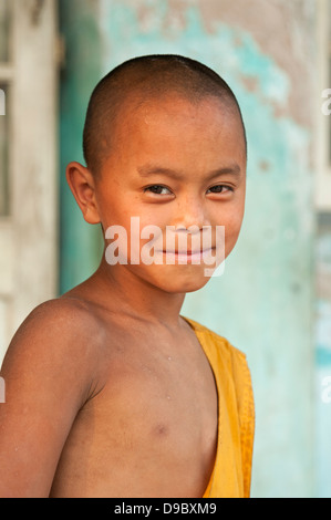 Garçon moine en robe jaune se trouve dans un temple porte le Myanmar Birmanie Banque D'Images