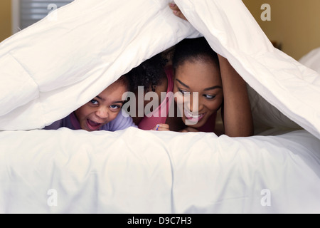 Mère et fille jouer sur lit de se cacher sous une couette Banque D'Images