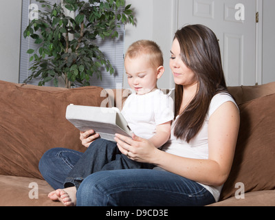 Pretty young Caucasian mère et son petit garçon blond assis à la maison sur le canapé lisant ensemble sur une tablette mobile sans fil. Banque D'Images