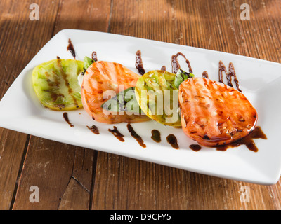 Bac blanc rectangulaire de salade caprese arrosée de vinaigrette balsamique reposant sur une table en bois rustique dans une lumière dorée. Banque D'Images