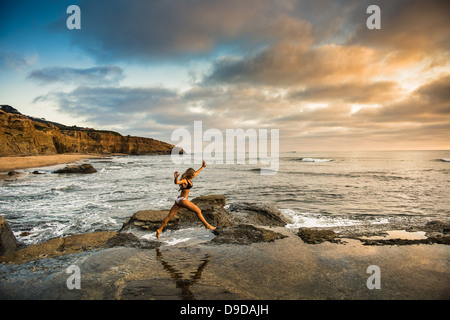 Young woman in bikini sautant de roches sur beach Banque D'Images