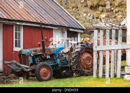 Vieux tracteur agricole est en norvégien à proximité village maison en bois rouge Banque D'Images