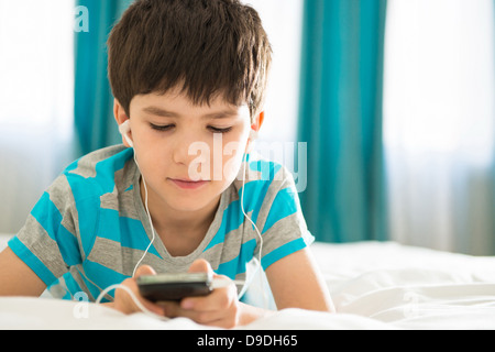 Boy listening to mp3 player on bed Banque D'Images