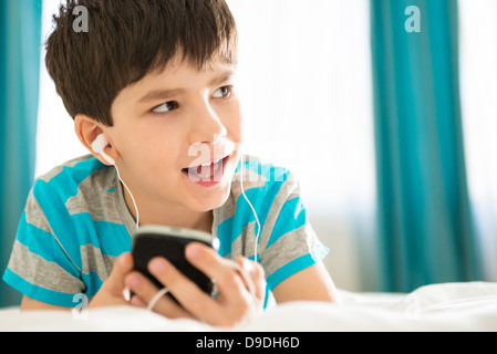 Boy listening to mp3 player on bed Banque D'Images