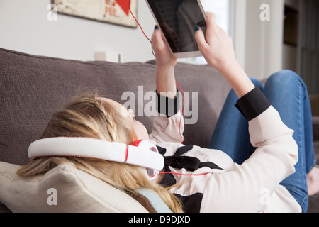 Girls lying on sofa using digital tablet Banque D'Images