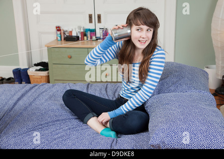 Girl sitting on bed jouant avec de l'étain peut téléphone Banque D'Images
