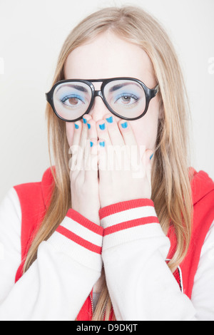 Girl wearing fake spectacles avec mains couvrant sa bouche Banque D'Images