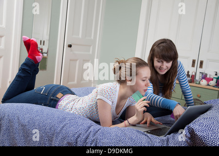 Girls lying on bed with laptop internet shopping Banque D'Images