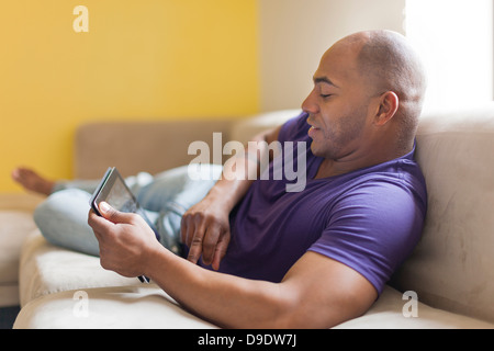 Mid adult male on sofa with digital tablet Banque D'Images