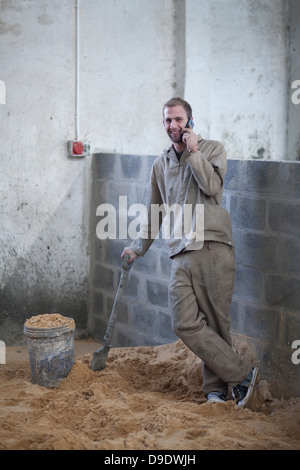 Homme debout avec spade talking on cellular phone Banque D'Images