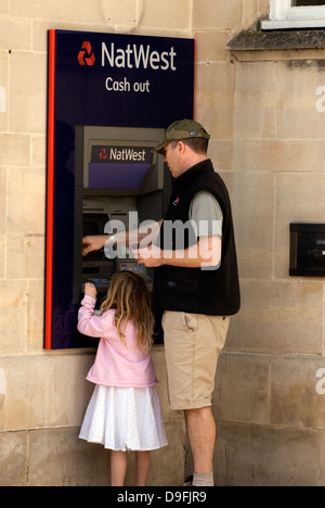 L'homme avec sa jeune fille à l'aide de la machine distributeur de Natwest, Petersfield, Hampshire, Royaume-Uni. Banque D'Images