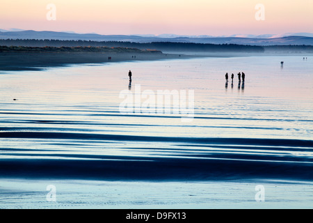 Silhouetté chiffres sur l'exploitation des sables bitumineux de l'ouest au crépuscule, St Andrews, Fife, Scotland, UK Banque D'Images