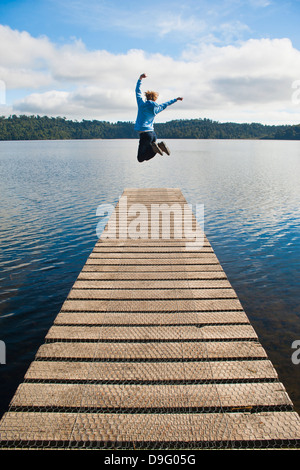 Femme sautant sur une jetée au lac Ianthe, West Coast, South Island, New Zealand Banque D'Images