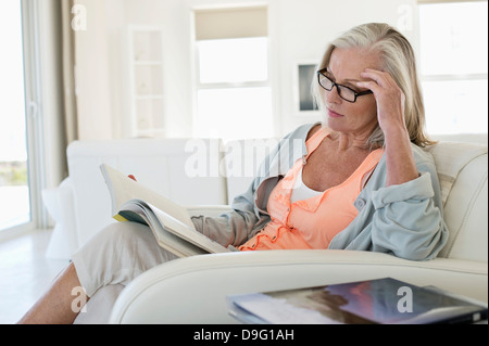 Femme assise sur un canapé et la lecture d'un livre à la maison Banque D'Images